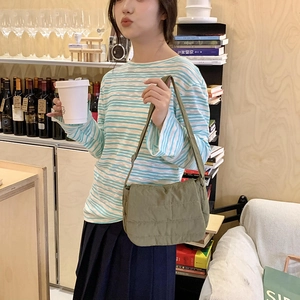 Detail of olive green quilted crossbody bag shown on a model in a warm cafe setting