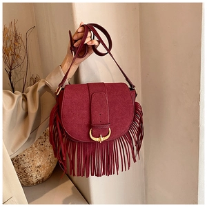 Detail view of burgundy matte saddle bag featuring bohemian fringe and gold metal buckle