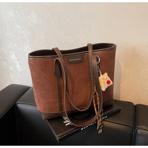 Detail of dark brown suede tote bag with leather trim and plush cartoon charm