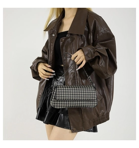 Close-up of houndstooth PU shoulder bag held by a model in a retro leather jacket