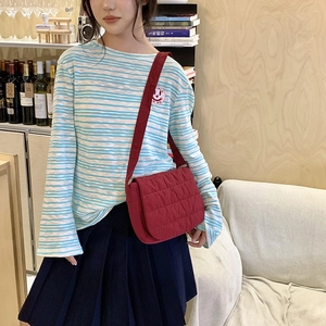 Detail of red quilted crossbody bag paired with blue and white striped long sleeve top