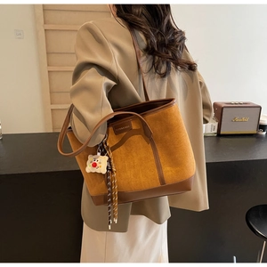 Detail of a large brown suede and leather patchwork tote bag with stylish fuzzy pendant