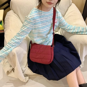Close-up of a red quilted crossbody bag with puffer texture and adjustable strap on a model