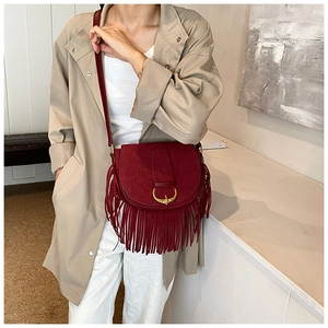 Detail of burgundy faux suede shoulder bag with gold horseshoe buckle and long tassels
