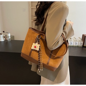 Detail of dark brown suede tote bag with leather piping and cute clown plush charm