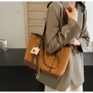 Detail shot of a dark brown suede tote bag with leather straps and plush charm on a model