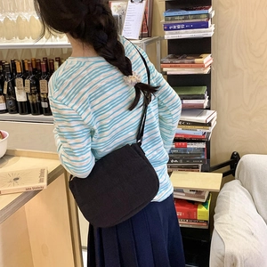Minimalist black canvas messenger bag detail with adjustable strap on a striped outfit