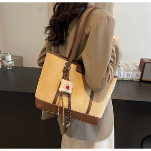 Detail view of khaki suede tote bag with brown leather trim and plush charm accessory