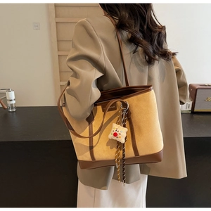 Detail of large yellow suede tote bag with brown leather trim and plush charm