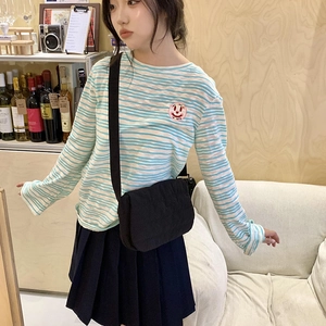 Detail view of a black fabric crossbody bag styled with a striped long-sleeve tee