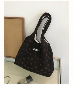 Détail du cabas en velours côtelé noir avec motif fraise rouge et étiquette en tissu blanc