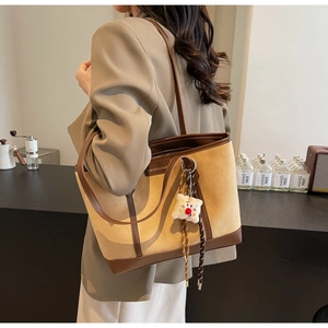 Detail of a large contrast tote bag in light brown suede with dark leather trim and plush charm