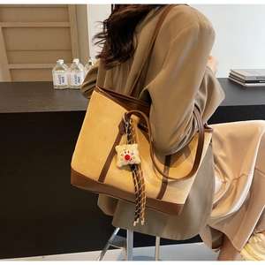 Detail view of a large brown suede patchwork tote bag with stylish plush doll pendant