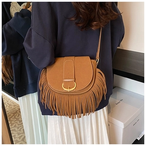 Detail of a brown suede saddle bag featuring long bohemian tassels and golden metal buckle