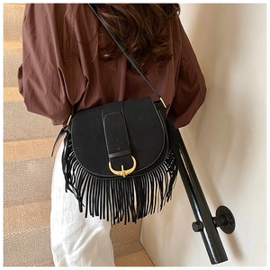 Detail of black matte saddle bag featuring long tassels and a large gold horseshoe buckle