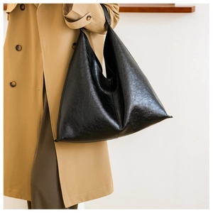 Chic black faux leather tote bag with glossy finish on a stylish model in a trench coat