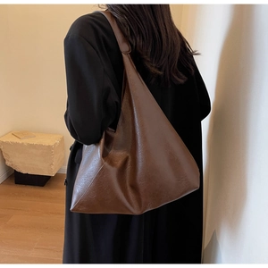Close-up of a large dark brown faux leather hobo bag on a model in a black coat