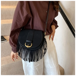 Detail of black faux suede crossbody bag with gold horseshoe buckle and long tassels