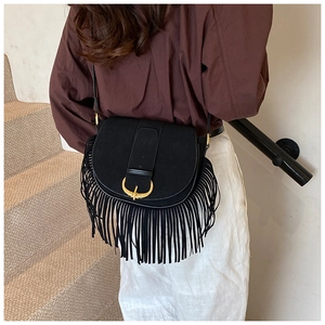 Detail of black matte saddle bag with bohemian fringe and golden horseshoe buckle