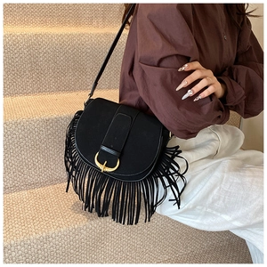 Detail view of black PU suede saddle bag with golden horseshoe buckle and long tassels