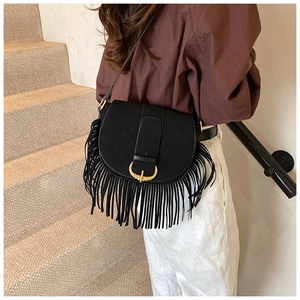 Detail of black suede saddle bag with long tassels and a vintage gold metal buckle