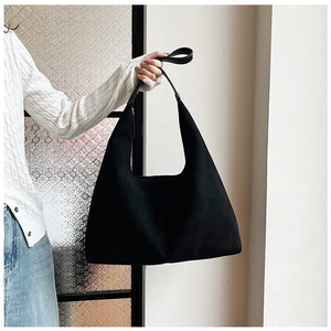 Minimalist large black matte PU leather hobo tote bag held by a model in a cozy interior