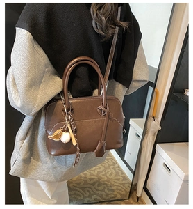 Detail of vintage brown PU leather handbag featuring unique baseball bat charm accessory