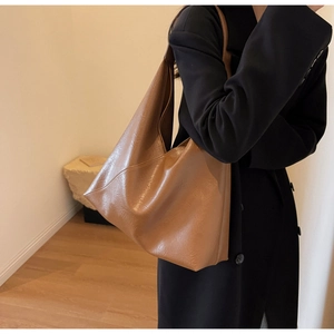 Detailed view of a brown minimalist faux leather tote bag worn with a black wool coat