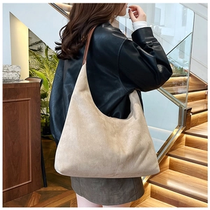 Detailed view of apricot suede tote bag with leather strap worn over a black jacket