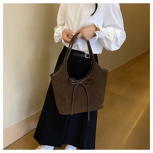 Détail d'un sac cabas en daim marron avec nœud en cuir et finitions de passepoil