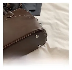 Detail shot of a dark brown PU leather shoulder bag with white stitching and silver studs