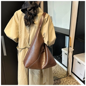 Detail of vintage oil wax leather shoulder bag in brown, styled with a trench coat