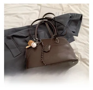 Detail view of brown vintage PU leather Boston bag with a sports-themed charm on bed