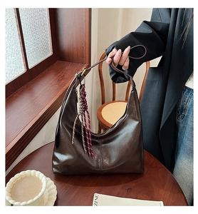 Detail of dark brown leather tote bag with woven knot pendant in a cozy cafe setting