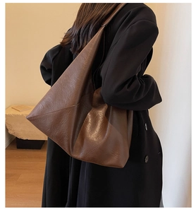 Side view of a large brown leather tote bag worn by a model in a modern interior