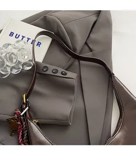 Detailed close-up of a brown leather hobo bag with braided key charm on a grey blazer