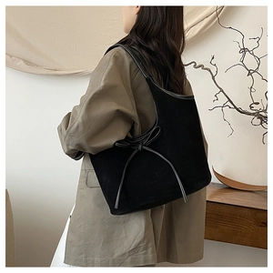 Détail du sac cabas en daim noir avec nœud en cuir porté par un mannequin en intérieur