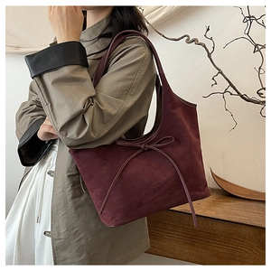 Détail du sac cabas bordeaux en daim avec un nœud élégant porté sous le bras