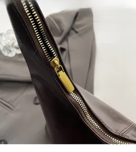 Close-up of premium golden metal zipper on dark brown leather handbag with fine stitching