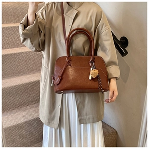 Detail of a dark brown PU leather shell bag with heart charm shown on a stylish model