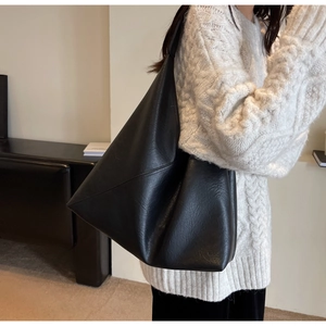 Detail shot of a black matte soft leather shoulder bag paired with a white knit sweater