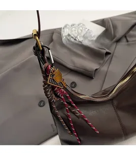 Detail of a dark brown leather bag showing a woven charm with a gold geometric pendant