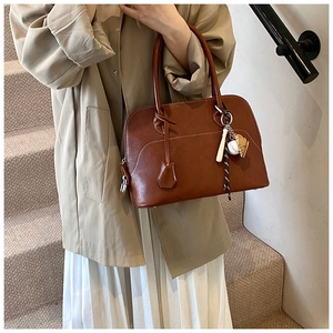 Detail of a brown PU leather shoulder bag with white contrast stitching and baseball charm