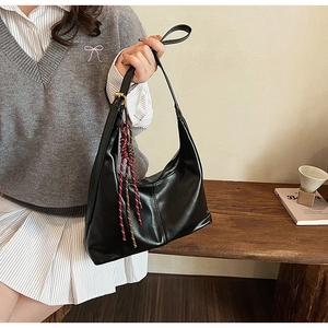 Detail of a black PU leather hobo bag with gold buckle and woven charm in a lifestyle setting