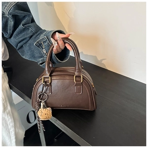 Detailaufnahme der dunkelbraunen Boston-Tasche aus PU-Leder mit Mini-Sneaker-Anhänger und Golddekor