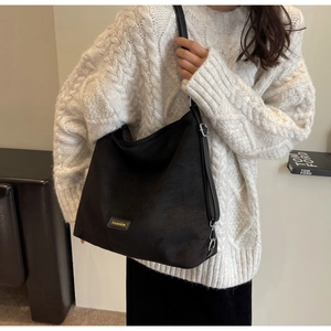 Close-up of a black faux suede hobo bag with yellow fashion label on white sweater