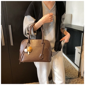 Detail view of brown PU leather shell bag with lychee texture and baseball charm on strap
