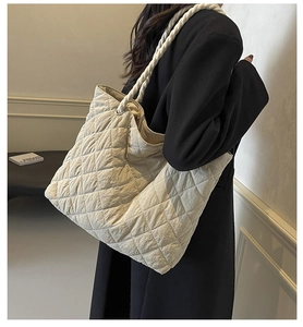 Detail of a beige quilted tote bag with braided rope strap on a model shoulder