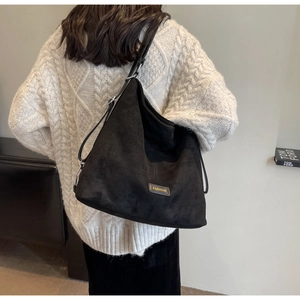 Close-up of black suede tote bag with fashion label on model wearing beige knit sweater