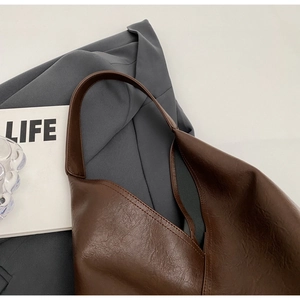 Detail of dark brown leather tote bag with lychee texture on grey suit blazer
